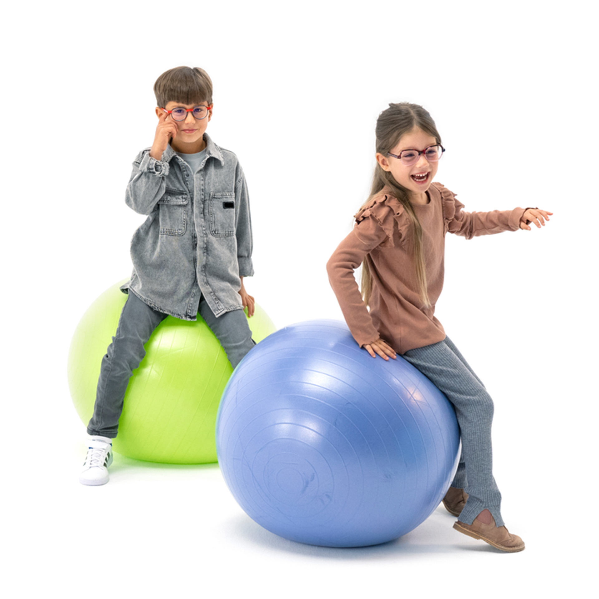 안경을 쓴 소년과 소녀가 공에 앉아 장난을 치고 있다.