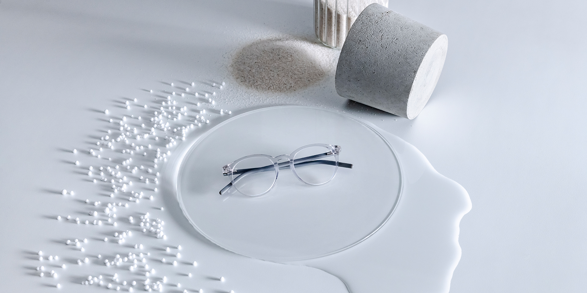 듀라비전® 코팅이 적용된 자이스 안경 렌즈가 물, 모래, 구슬, 돌로 둘러싸인 유리 받침대 위에 놓여 있다.