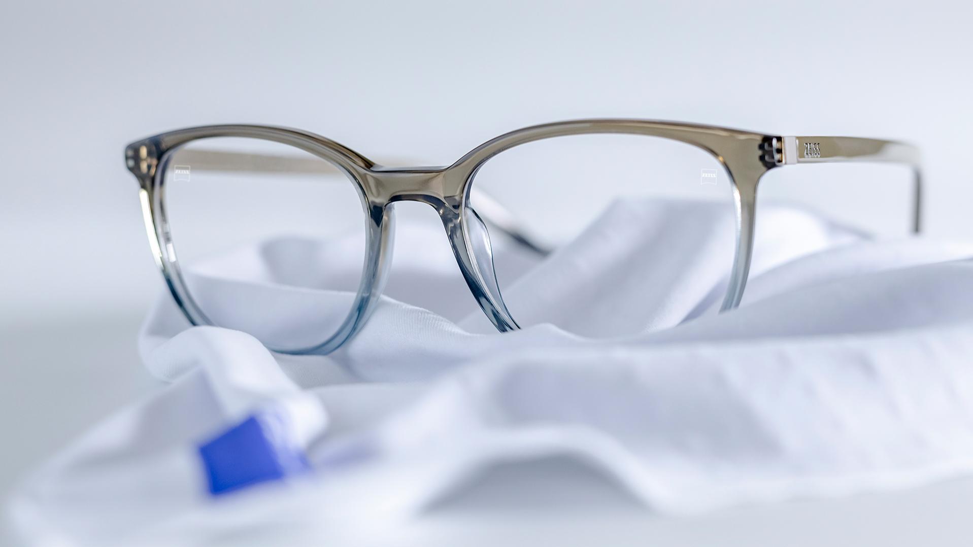 한 벌의 안경이 흰색 극세사 천에 놓여 있다. 회청색 프레임에 자이스 렌즈가 장착되고 렌즈에는 듀라비전® 코팅이 적용되어 있다.