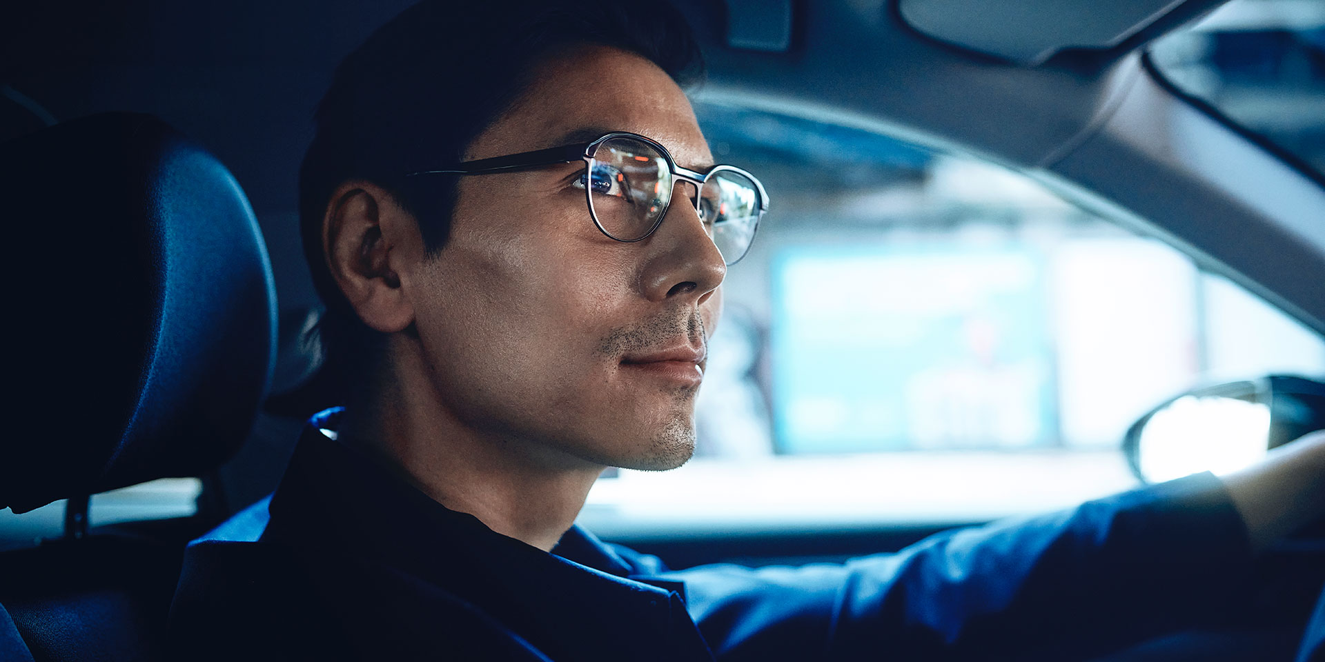자동차를 운전하는 남성이 운전 중 약간 미소를 띠고 있으며 자신감 넘쳐 보인다. 자이스 드라이브세이프 단초점 렌즈를 착용하고 있다.