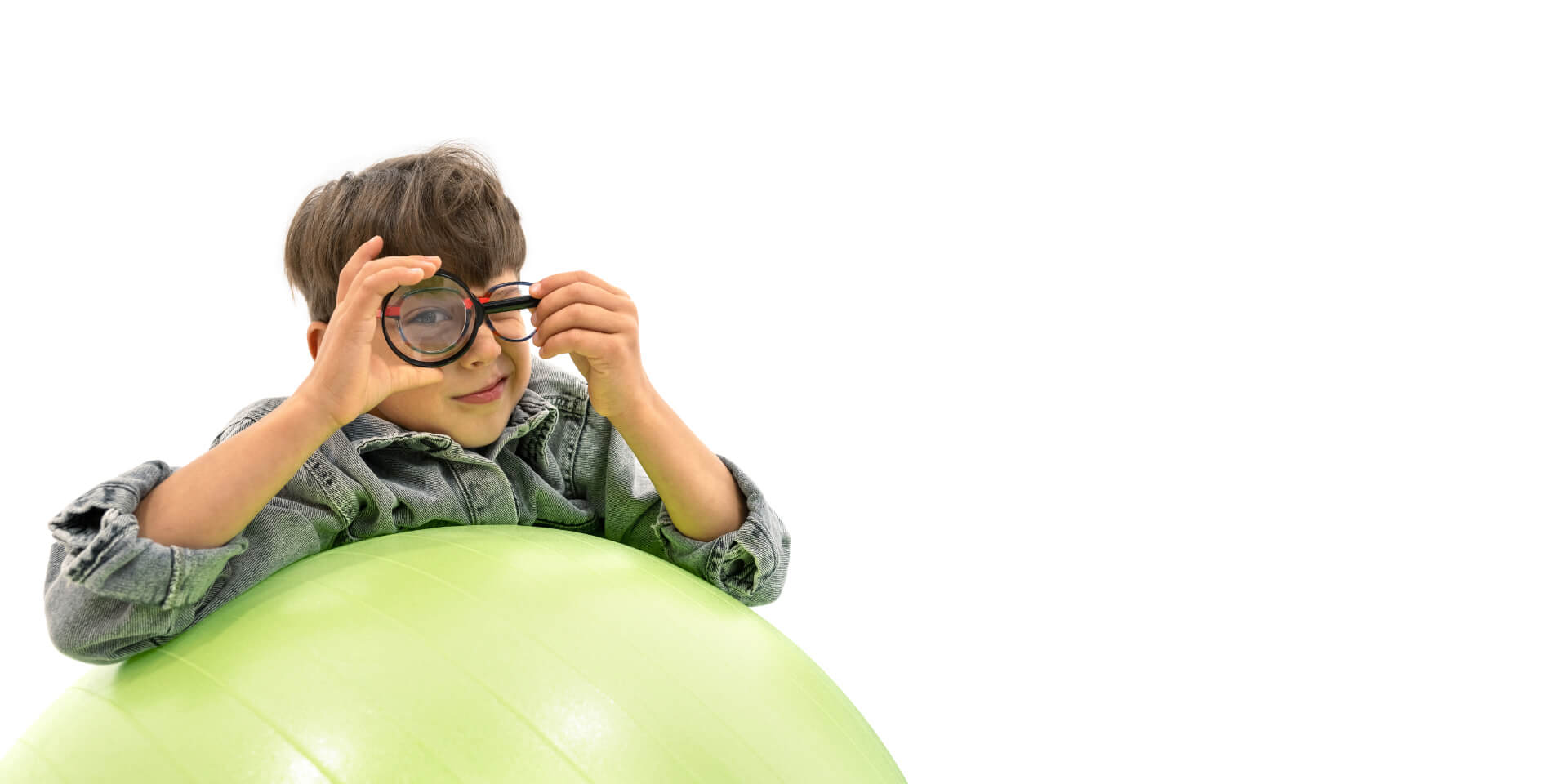 자이스 근시 관리 렌즈를 착용한 소년이 체조 공에 몸을 기대고 눈 앞에 확대경을 들고 있다.