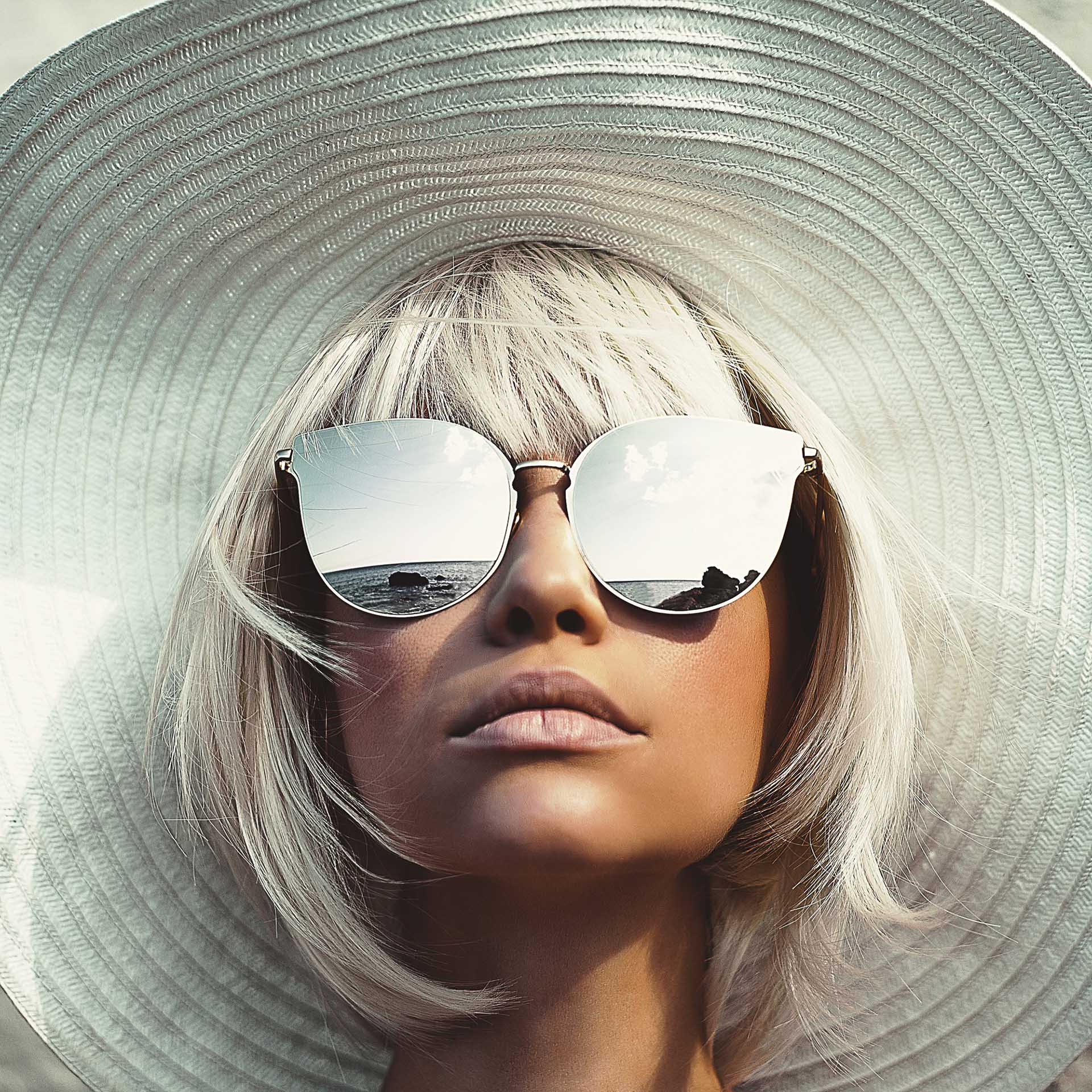 햇빛 차단 모자를 쓴 여성이 미러 효과가 있는 선글라스를 착용하고 위를 올려다보고 있다.