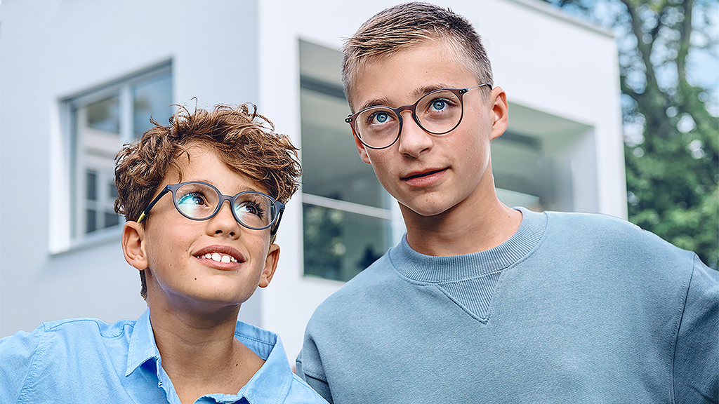 어린 소년과 십대 소년이 위를 올려다보고 있다. 두 소년 모두 자이스 스마트라이프 단초점 영 렌즈 안경을 착용하고 있다